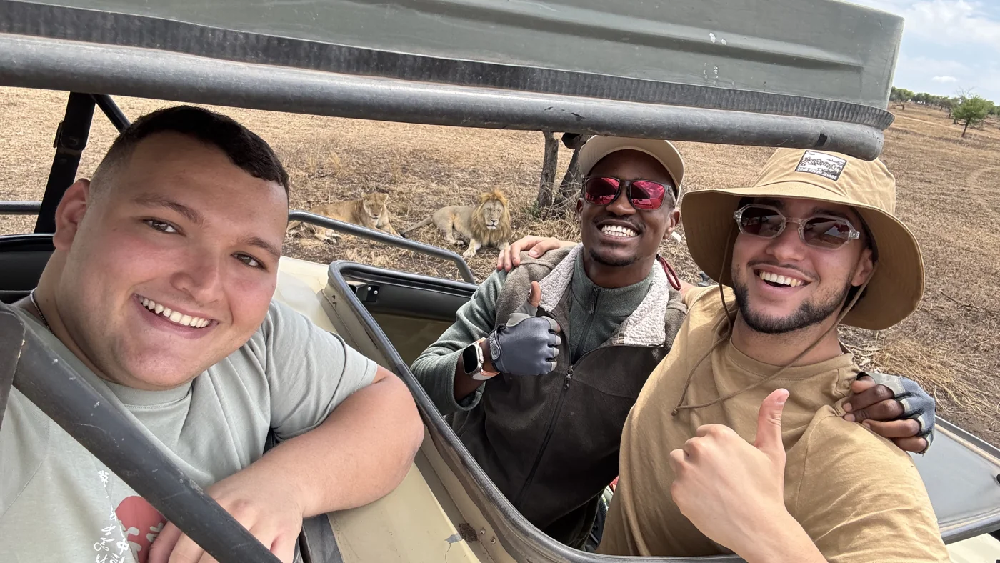 Three smiling safari guests in a vehicle with lions in the background